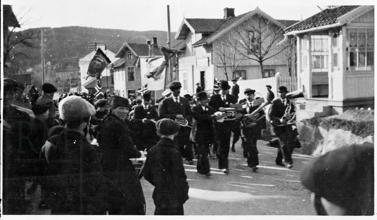 Musikkorps foran 1. mai tog med faner og flagg i Storgata på Nesbakken.