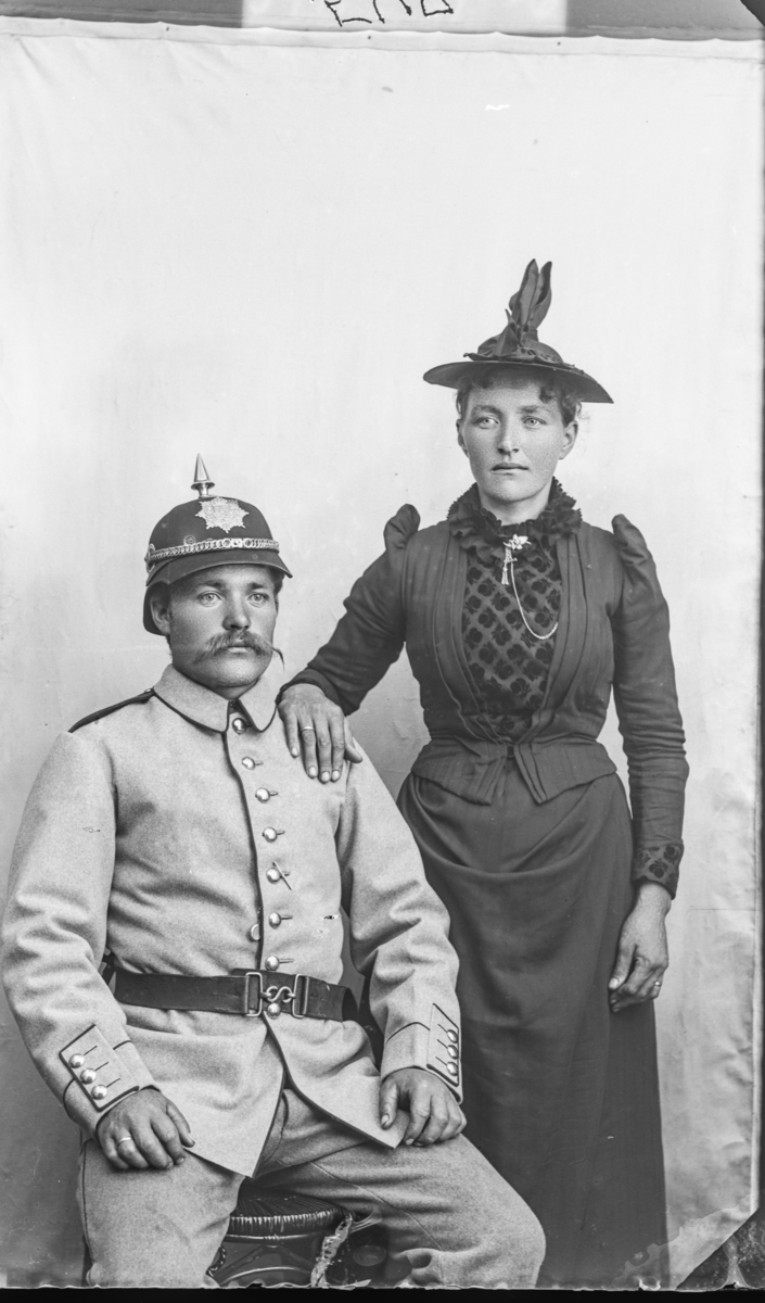 Familie Med Mann Som Sitter Og Dame Som Står Han Har Uniform Og Hjelm Modell 1888 For Hæren 