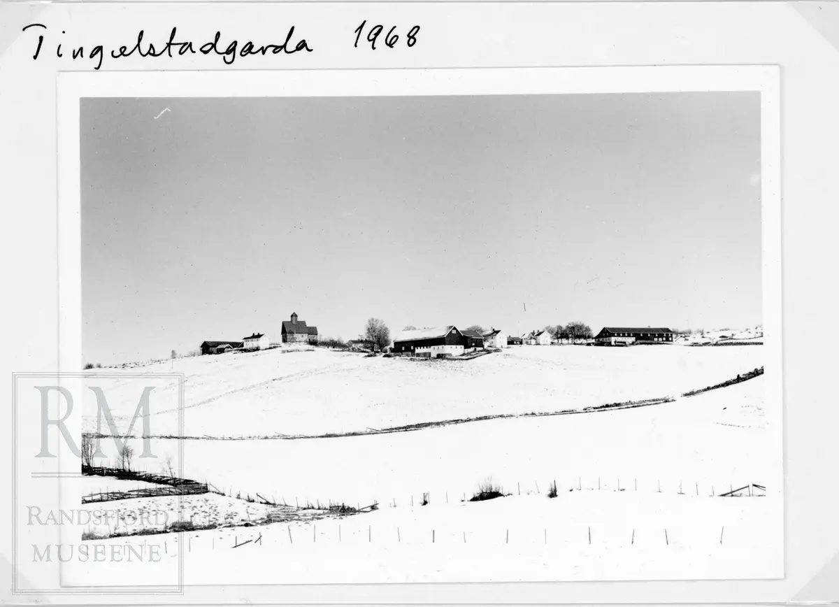 Tingelstadhøgda med gårder og snødekt mark. Tingelstad gamle kirke omkranset av Tingesltad gårder på toppen.