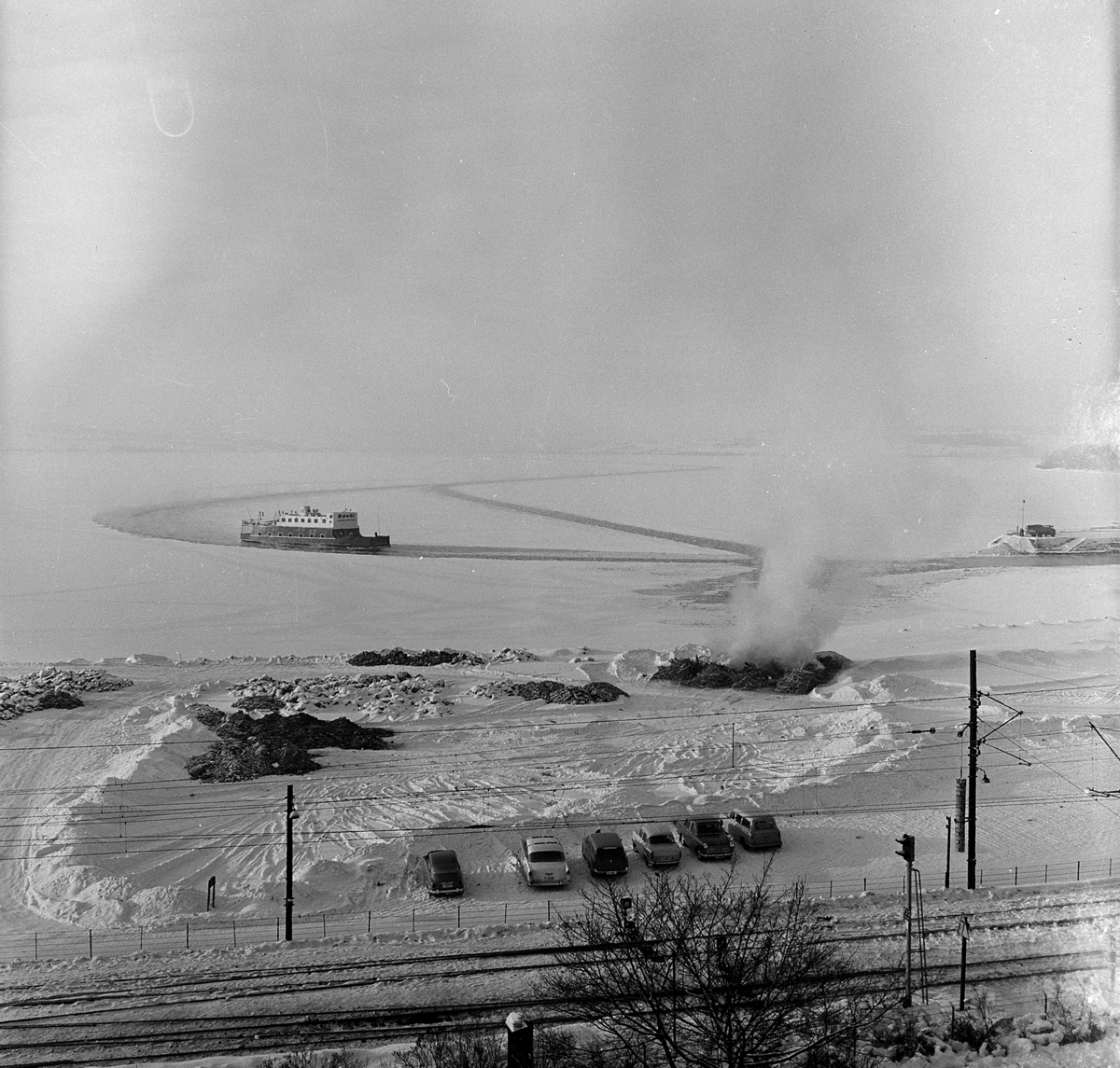 Hamarbukta, Hamar-Kapp Ferjen, mjøsbåt, i råk i mjøsisen, utenfor Hamar Brygge, senvinteren 1967. Bål, avfallsbrenning, bygningsrester åttemetersplanet. 
