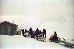 Gruppe med mennesker på fjelltur med snøskuter samlet ved hy