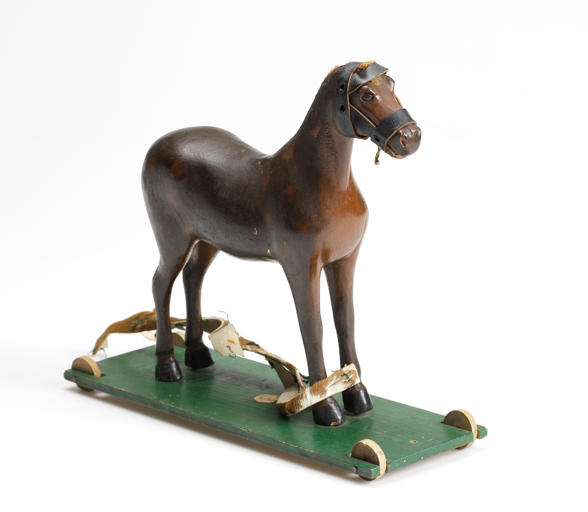 En leksakshäst av trä, stående på en grön platta med hjul.