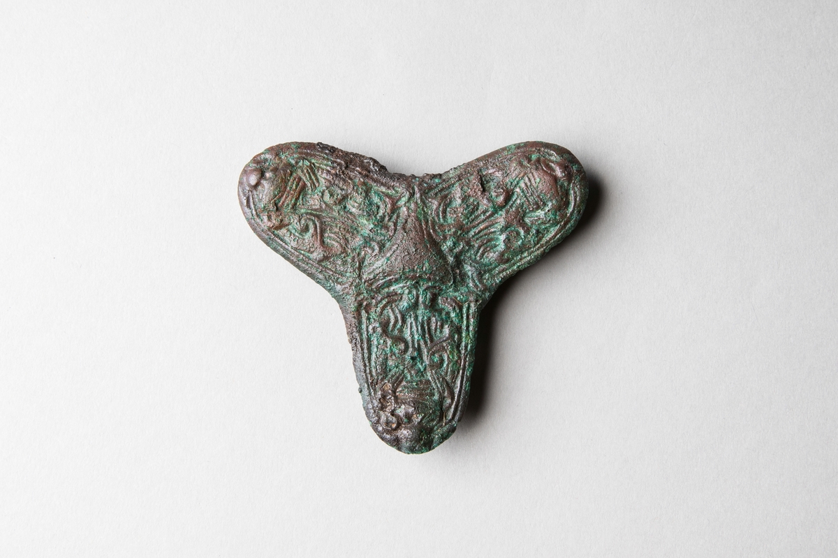 Treflikspänne av brons med ovansida dekorerad med en likformigt uppbyggd djurstilornamentik kring triangulär upphöjning med insvängda sidor. Undersida med nål av järn och nålhållare av brons. Spännet påträffades i en kvinnograv, troligen anlagd under första hälften av 9000-talet.