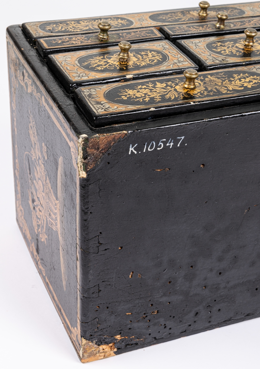 Kat.kort:
Skrin, kinesiskt lackarbete i svart, guld och silver, med landskapsbild och växtornament. Innehåller 9 små lådor, av vilka en är smal, sträckande sig över hela schatullets längd. Några av lådorna äro indelade i fack. Innuti klädda med rödaktig sammet. På undersidan av vänster låda nertill är skrivet "Philip Berhard Hebbe...1772" /el. 1779?/. Gästrikland.