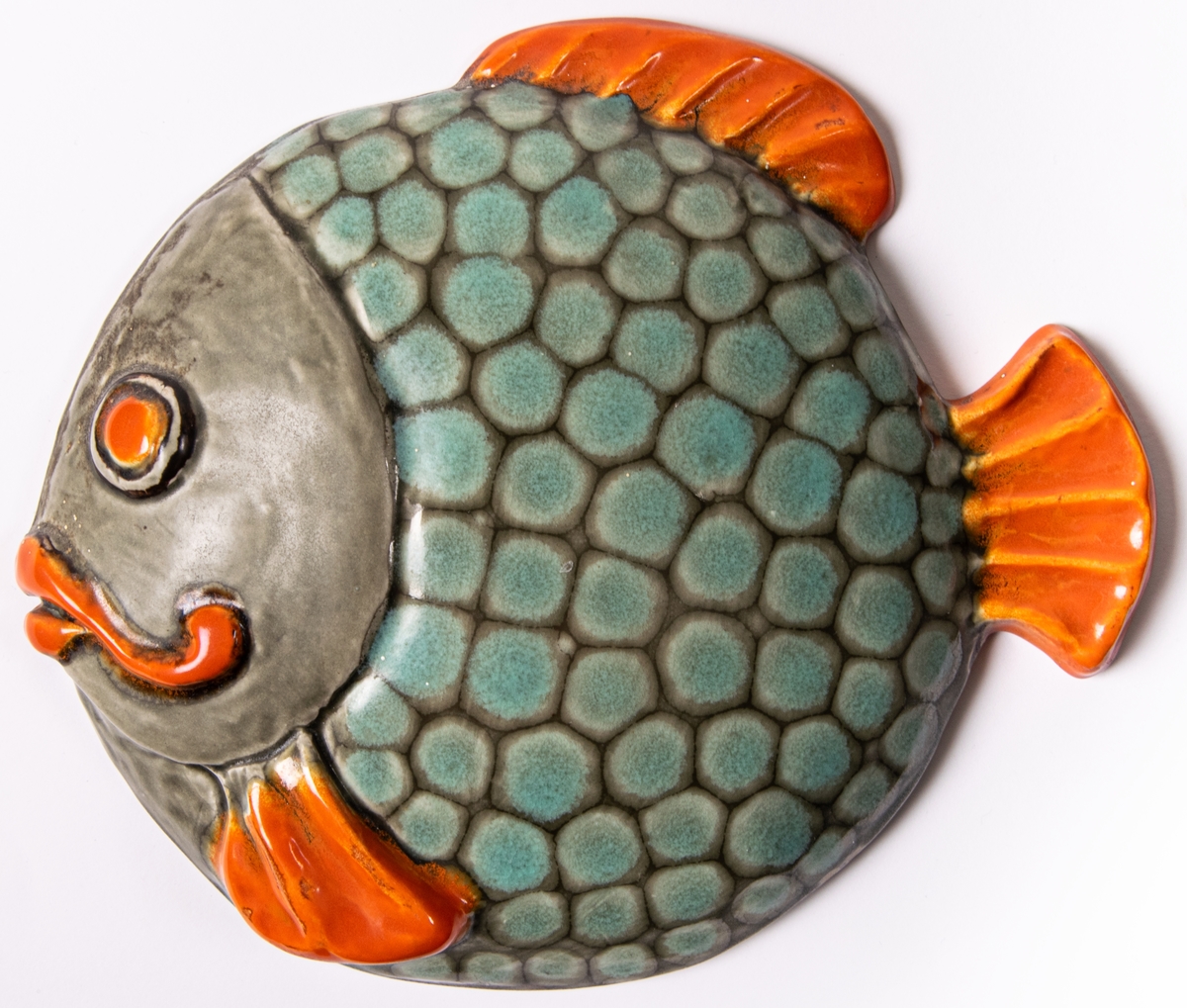 Väggfigurin i lergods i form av en fisk. Modell H.12 (angivet på baksidan) eller HO12 (enligt förteckning), glasyr 508 i orange, blekgrön och ljusbrun. Glasyren 508 användes enligt Birgitta Lundblads bok 1934-48.