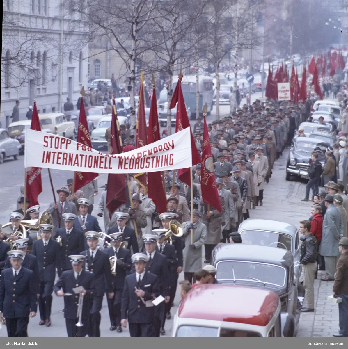 1 maj-demonstration 1959, med plakat och fanor på Köpmangatan samt stor folksamling på torget.