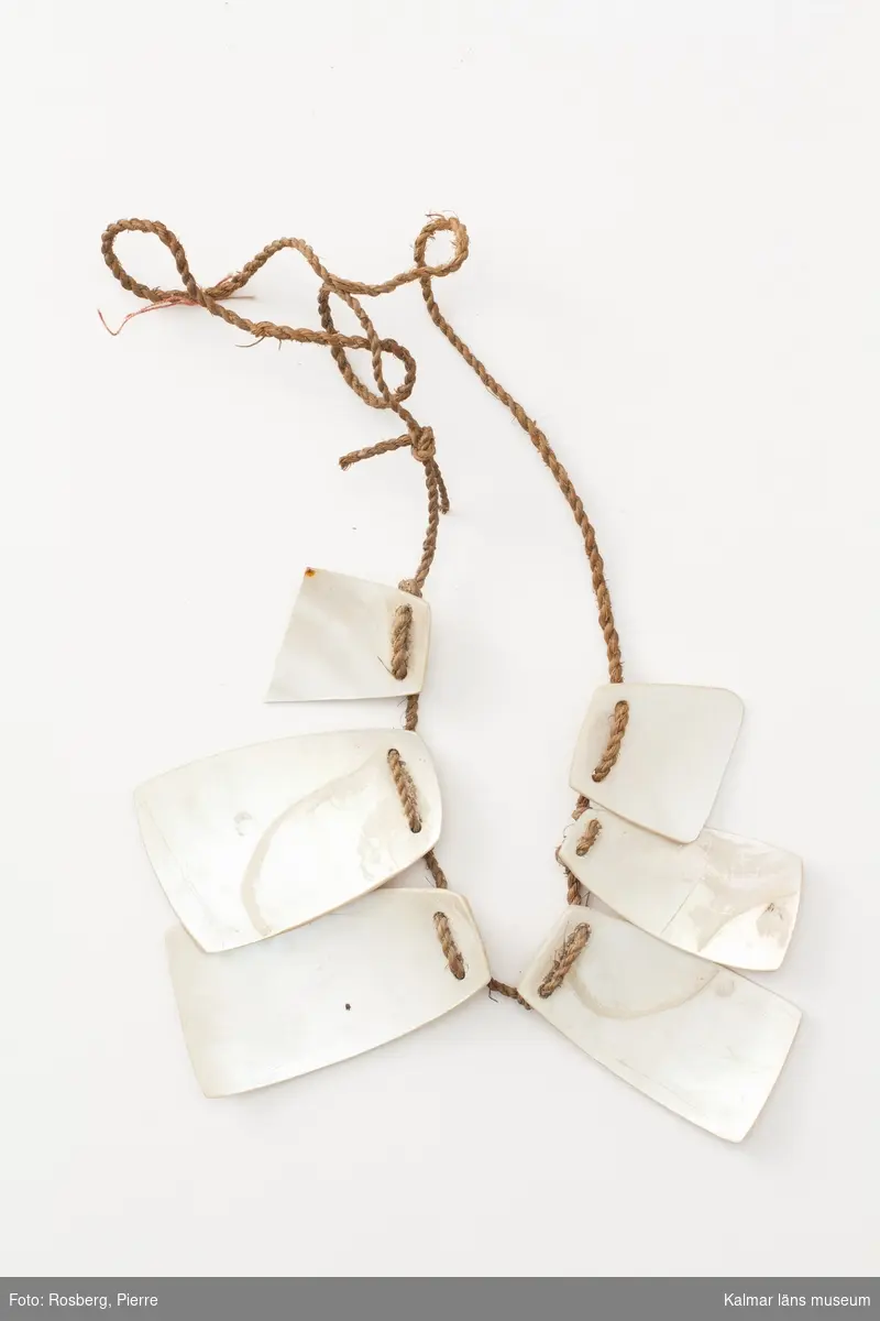 KLM 4056. Halsband av pärlemorskivor. Halsband av sex stycken tunna pärlemorskivor, uppträdda på ett snöre av bastfibrer. En skiva är brusten mitt av.
