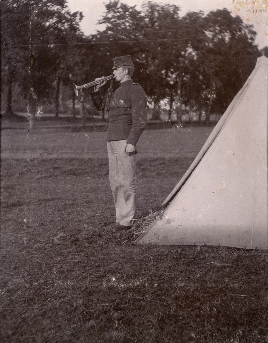 Soldat från Fortifikationen blåser trumpet utanför tält.