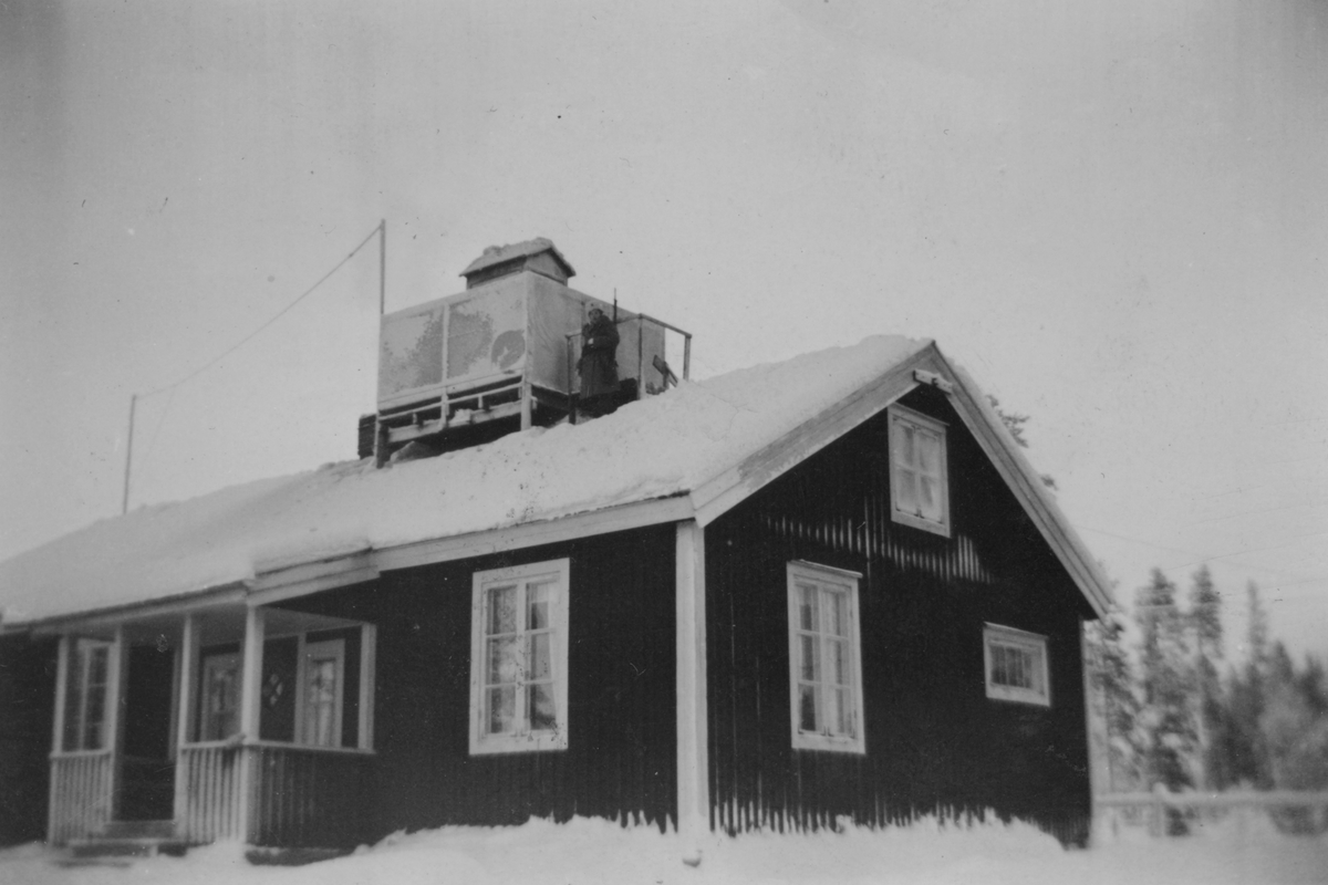 Exteriör av militärförläggningen för 91:a ls-kompaniet för luftbevakning i Tellejåkk, Kåbdalis under beredskapen, 1942. Ett hus med luftbevakningstorn på taket. På taket står en kvinnlig luftbevakare.