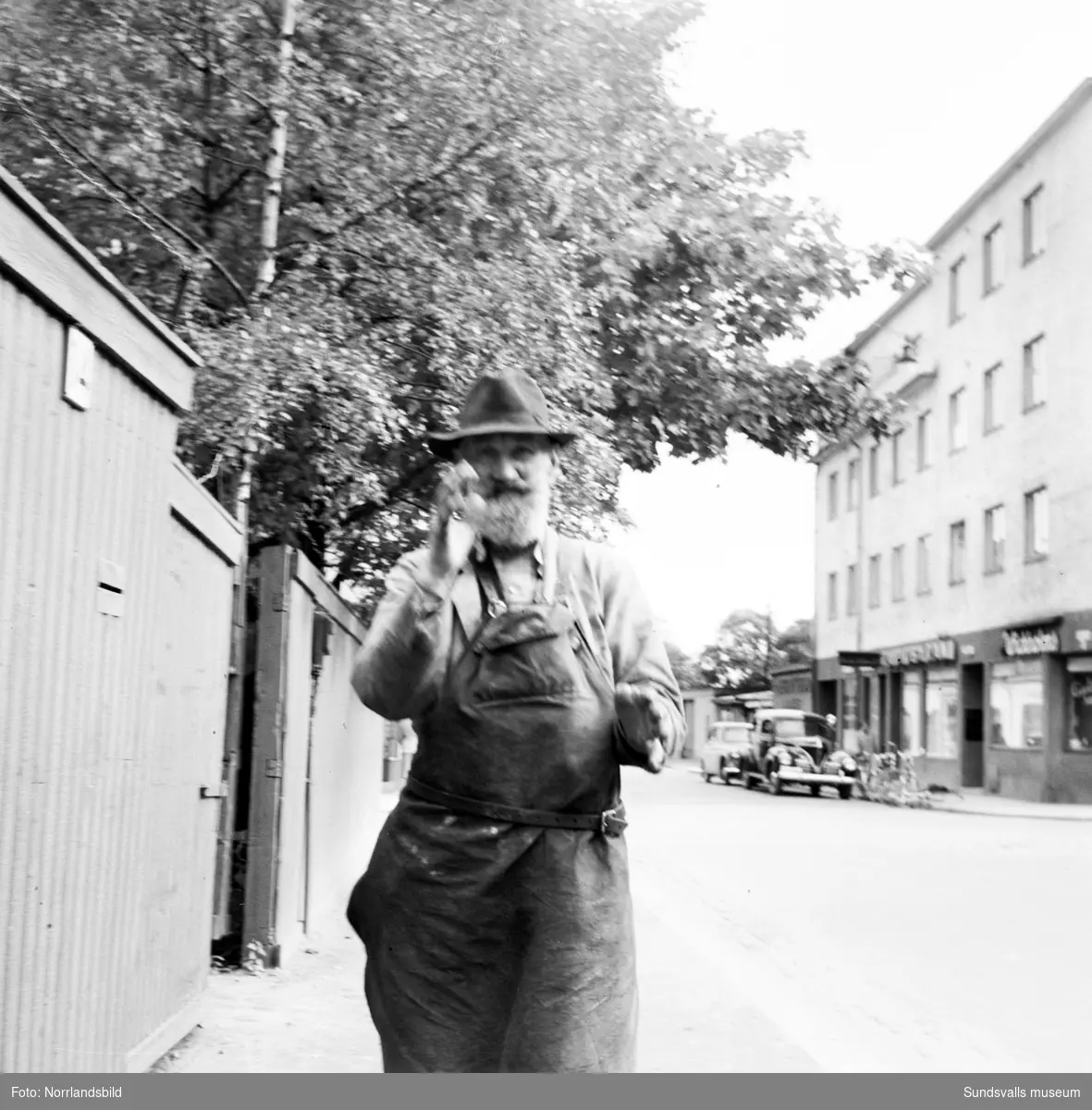 En skäggig man med arbetsförkläde kommer gående mot fotografen på Trädgårdsgatan. I bakgrunden syns huset vid Trädgårdsgatan 11.