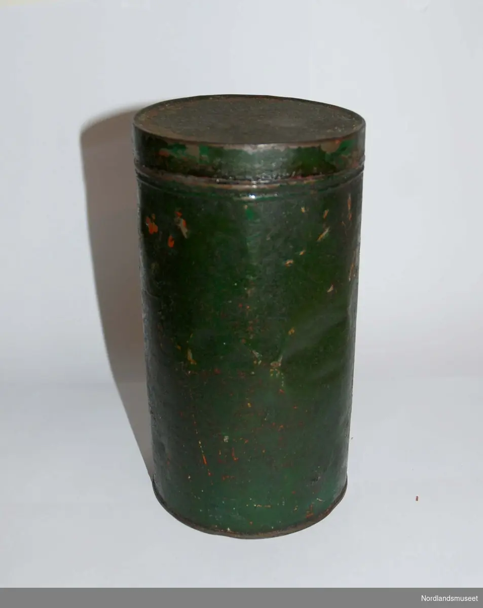 Rund kaffeboks med lokk i metall. Boksen er malt mørk grønn. Boksen har en del bulker og hakk. Litt rust.