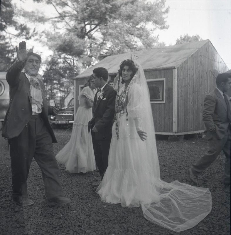 Nygift romskt par vid bröllop, november 1958 i Nyköping. Äldre romsk man välsignar paret. I bakgrunden syns uppställda vagnar, baracker och bilar i lägret.