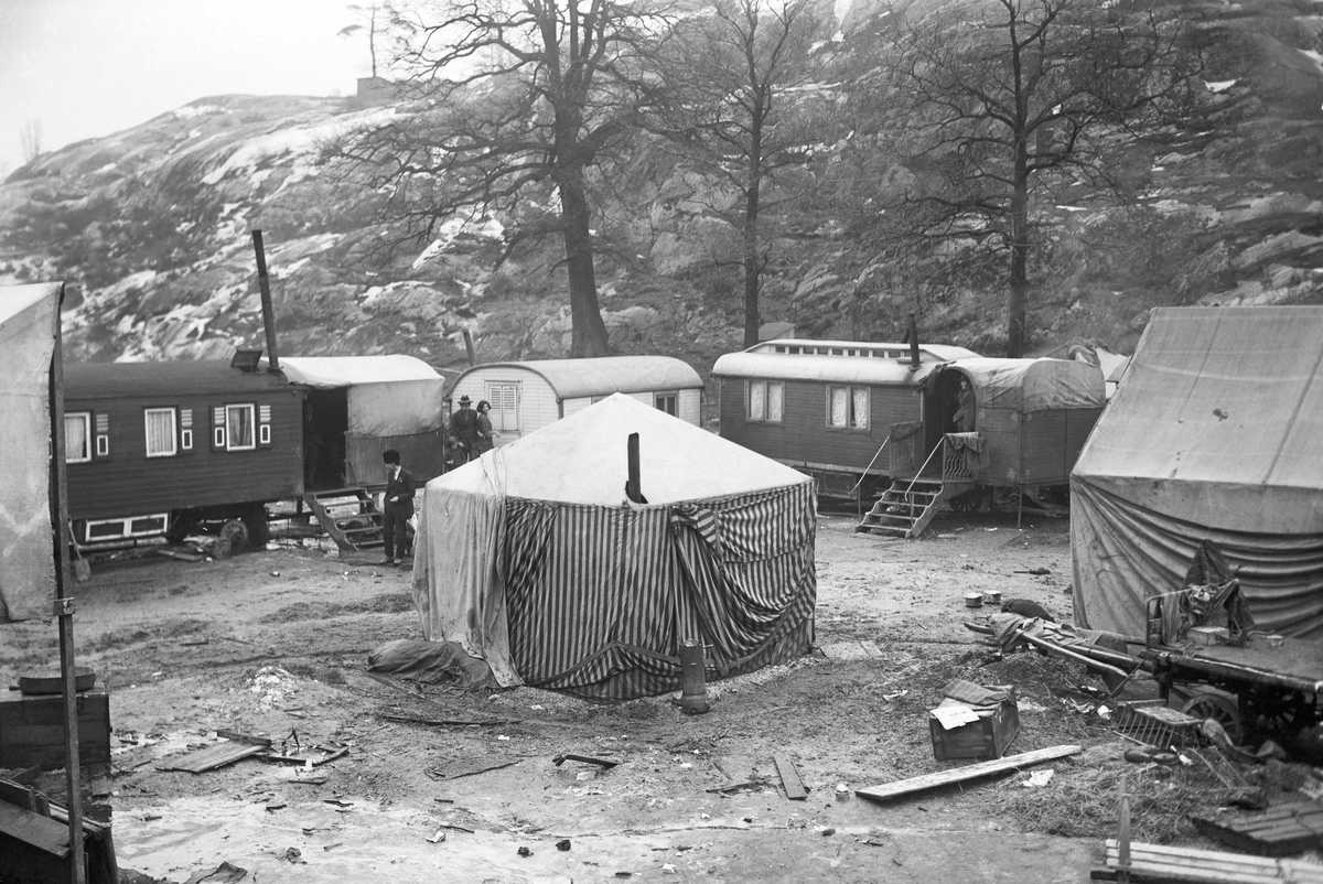 Ett romskt bostadsläger utanför Stockholm. I lägret står vagnar i en cirkel runt en "gårdsplan" som har ett tält i mitten.