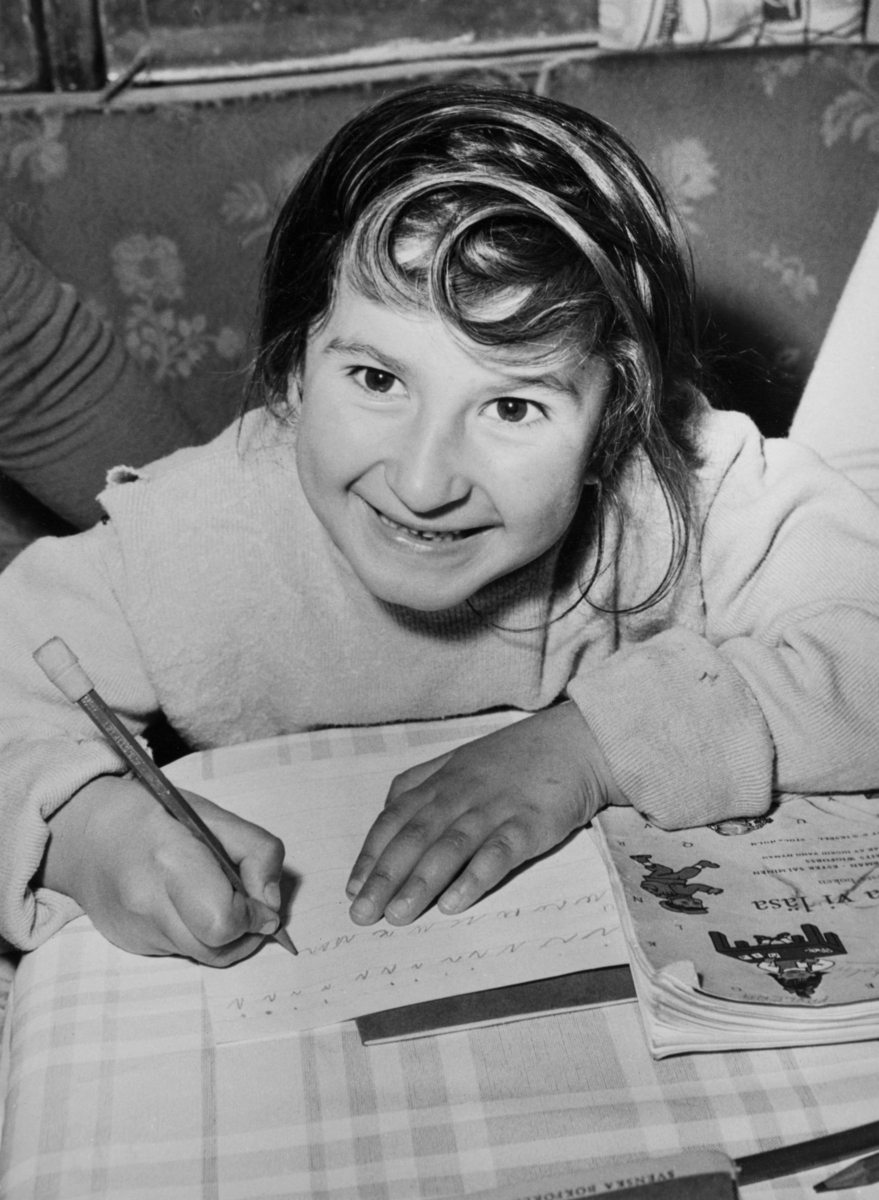 En flicka sitter i en bänk och skriver under sommarskola 1958.