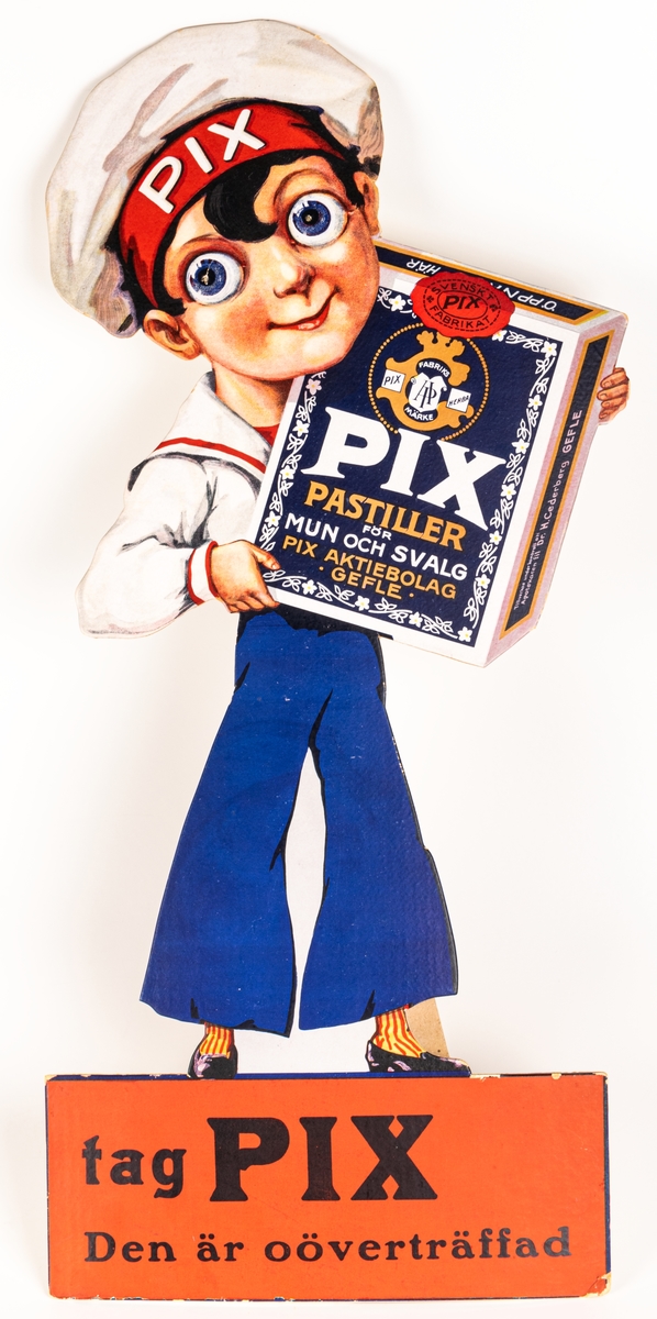 Reklamskylt i kartong. Skylten föreställer en pojke i sjömanskläder som bär en tablettask med PIX. Skylten går att ställa upp.