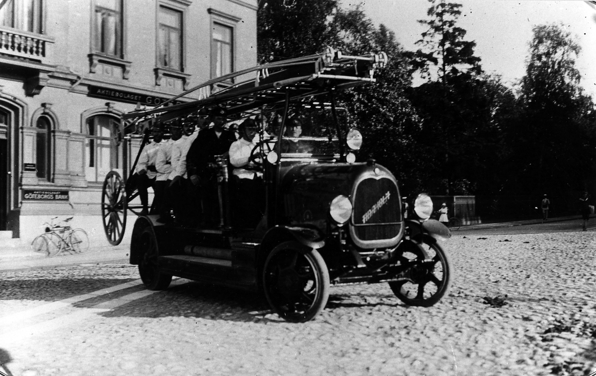 Brandkårens brandbil, inköpt 1921, fotograferad på Lilla Torget i Alingsås. Brandchefen Hjalmar Möller sitter bredvid chauffören.