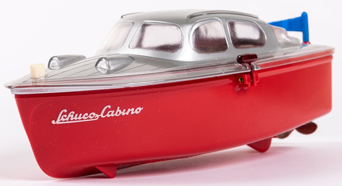 Leksaksbåt av gjuten hårdplast. Rött skrov och grått däckparti. Drivs med batteri. Ett batteri finns kvar. Båten ligger i orginalförpackning med bruksanvisning på engelska. Modell Cabino 5511. Tillverkad av Schuco i Tyskland.