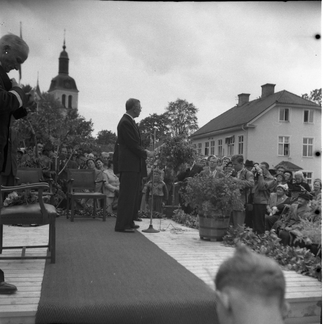 Eriksgata 1954. Kung Gustaf VI Adolf står på en särskilt uppbyggd estrad i Braheparken och talar till en folksamling. Närmast till vänster skymtar landshövding Olle Ekblom.