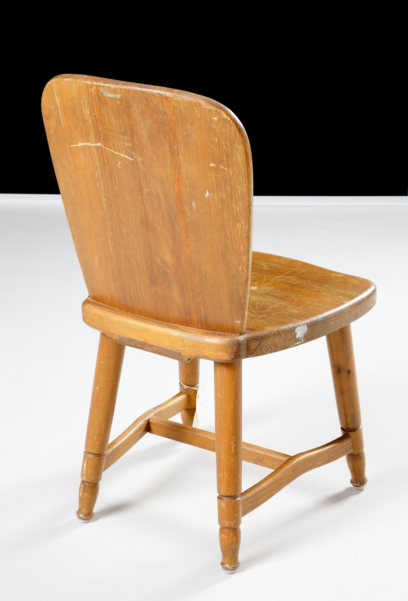 En enkel stol i fernissad furu med hel rygg och fyra ben.