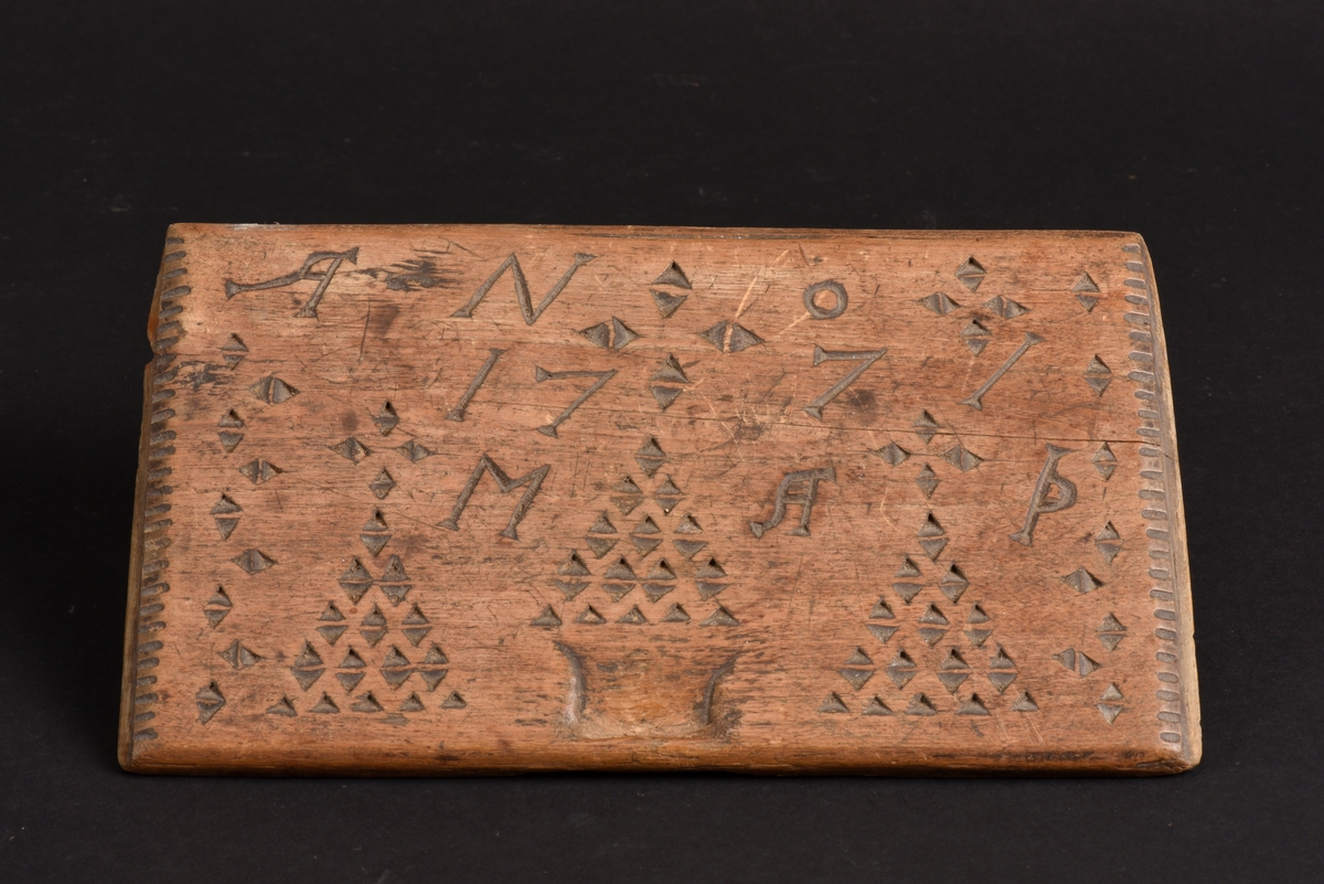 Kryddlåda av trä och skjutlock. Lådans yttre är skuren i ett stycke och har en inredning med sex fack. Skjutlocket har geometriska mönster i form av trianglar samt årtalet 1771 och initialerna MAD inskuret.