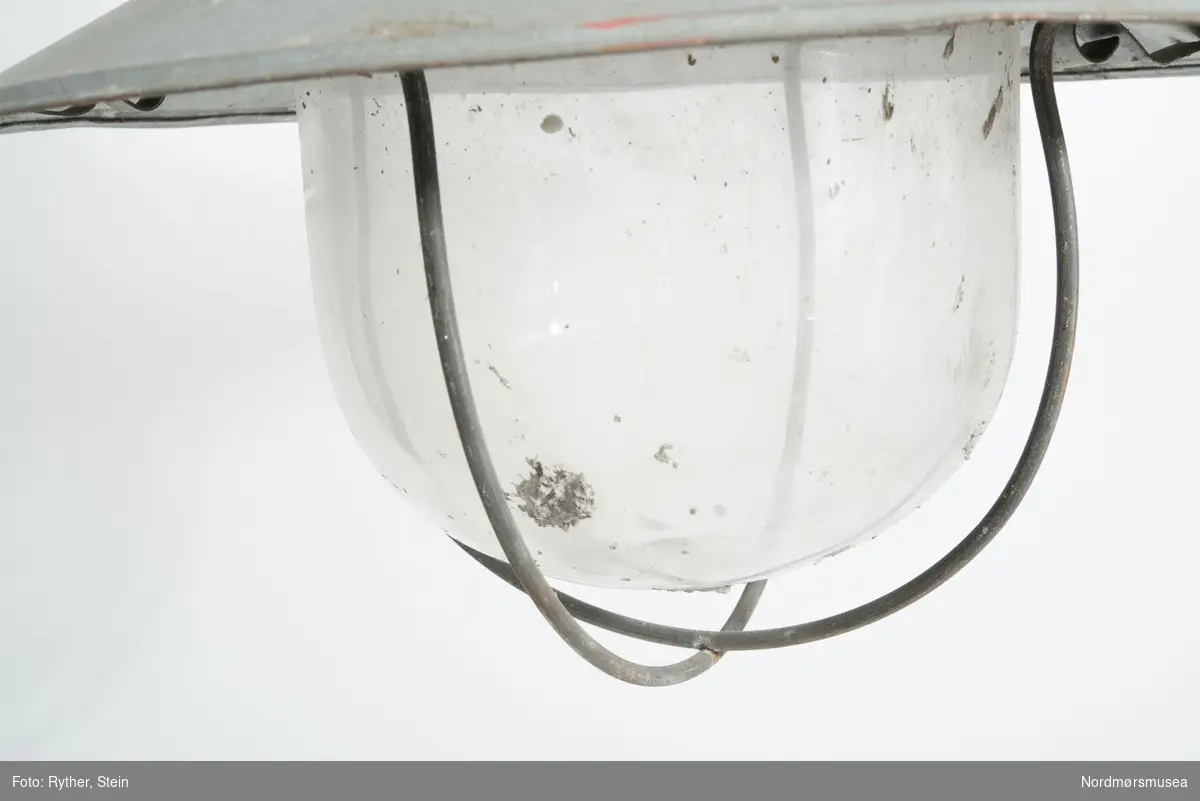 BESKR: Korslagte tråder som bøyle under glasskuppelen. Ledning surret rundt toppen. Hank til å bære i.

BRUK: Jf. KM.04445 og 04447. Lampa er omgjort til elektrisk lampe seinere.