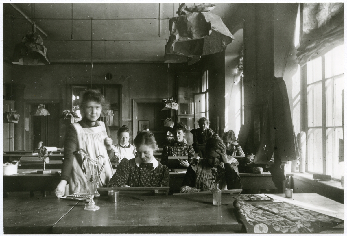 Stockholm. 
En grupp kvinnor. Sittande kvinnor ritar vid "skolbänkarna". 1901.