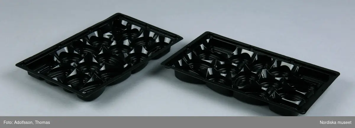 2 st brickor/formar hörande till chokladask. Av svart plast (polyetylentereftalat, PET), varje bricka med 16 st platser för praliner. I materialet (formpressat) symbol för att plasten kan användas för matvaror i form av bägare och gaffel, Produktnummer "1571029", samt symbol visande vilken sorts plast det är: Trekant av pilar med 01 inskrivet i mitten, under" A-PET"
/Leif Wallin 2015-01-12