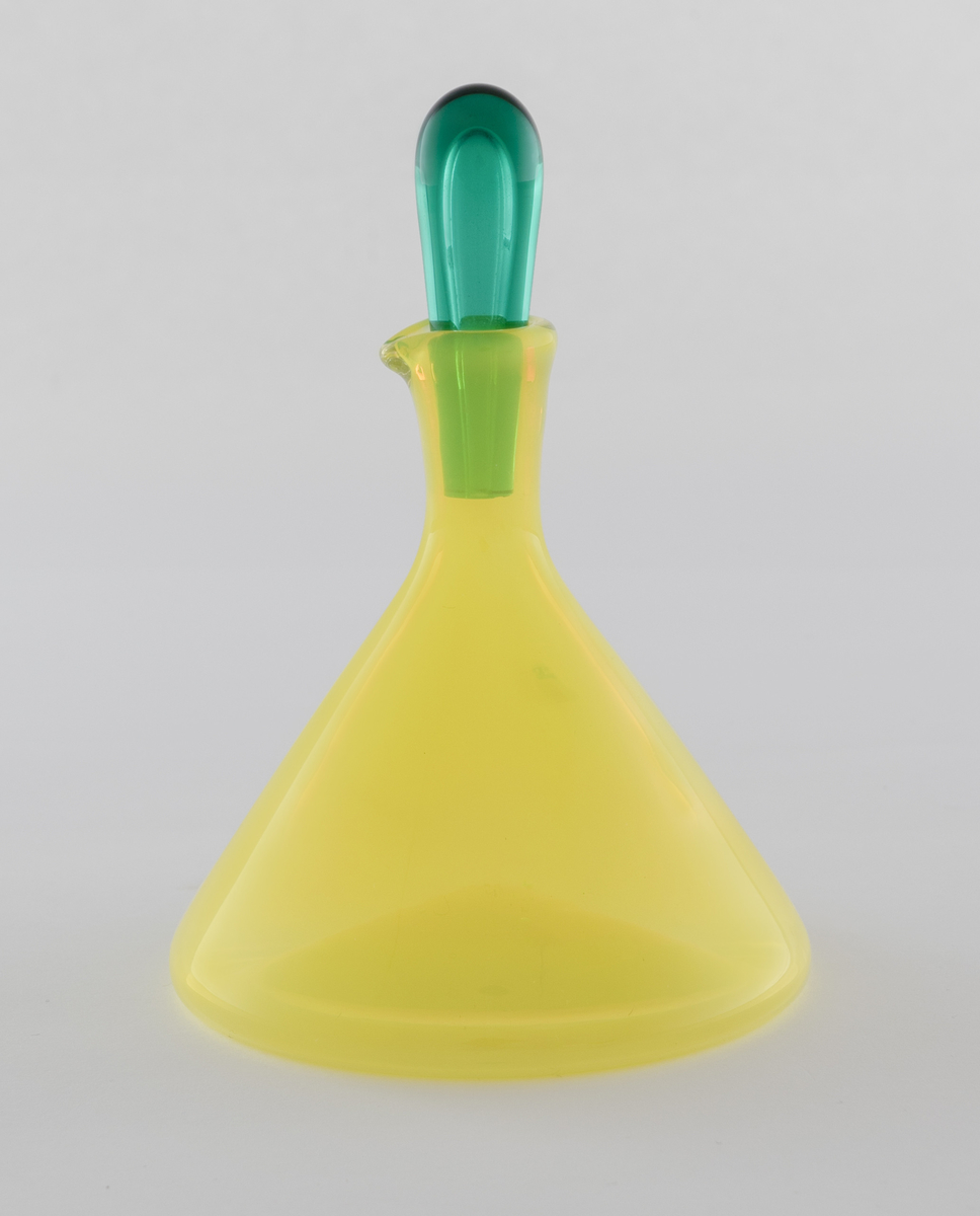 Edikk- eller oljekaraffel med propp i farget glass. Konisk koprus i halvgjennomskinnelig gulfarget glass, som avsluttes i en smal hals med tut. Den dråpeformede proppen er utført i gjennomskinnelig grønnfarget glass.