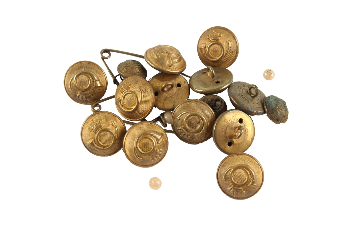 15 knapper til postmannsuniform, oppbevart i en skyveeske. Motiv av et posthorn på knappene.