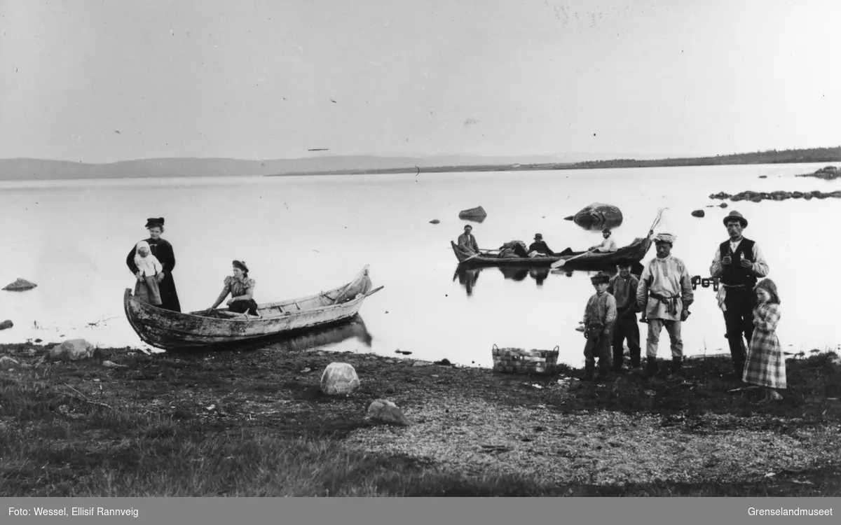 Pasvikelva ved Svanvik/Salmijärvi i 1890-årene. En båt ligger ved elvebredden med to kvinner og et barn i. En båt ligger ute på elva med tre menn ombord. Fire barn og en mann står på elvebredden.