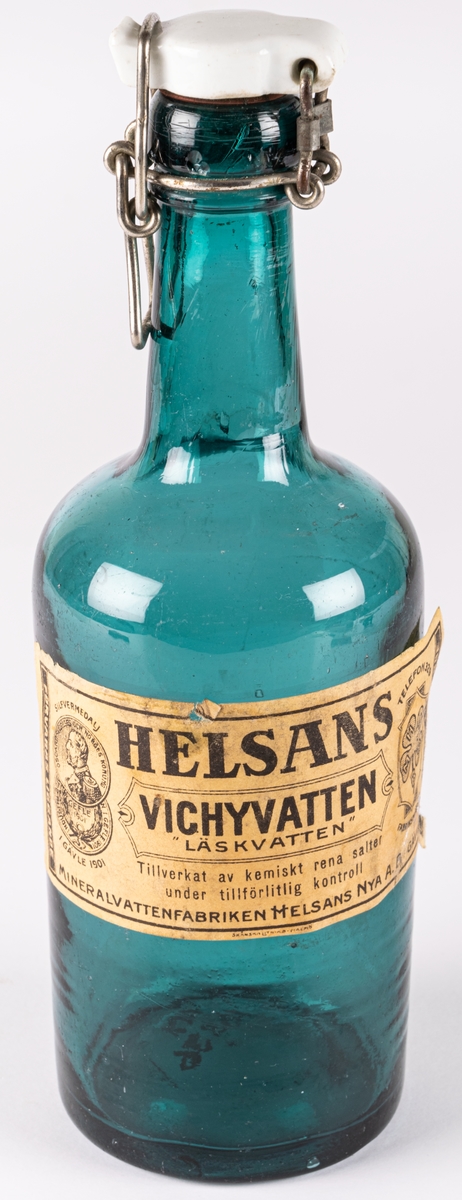 Vichyvattenflaska, grönt glas. Etikett från Mineralvattenfabriken Helsans Nya A.B. Gävle. Vit emaljkork.