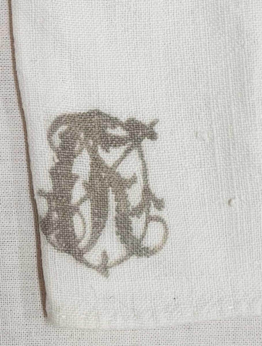 Bunadsskjorte av lin med hullsøm lang åpningen midt foran. Monogram nederst på høyre forside.