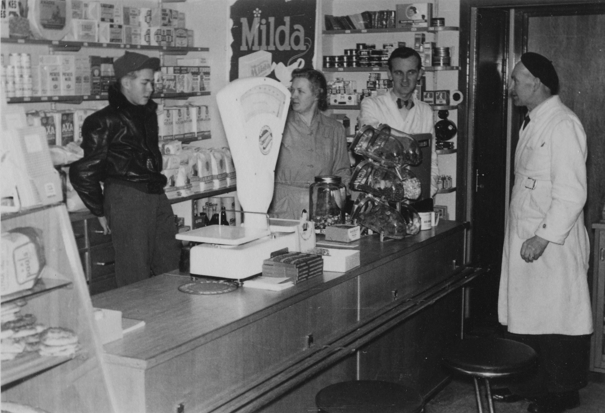 Från vänster: Ove Kjell-Svärd - Margit Kjell - Arnold Andersson - Edvin Kjell fotograferad i Kjells speceriaffär som låg i hörnet Hemvägen - Lärkvägen. På väggen bakom dom en reklamskylt för Milda.