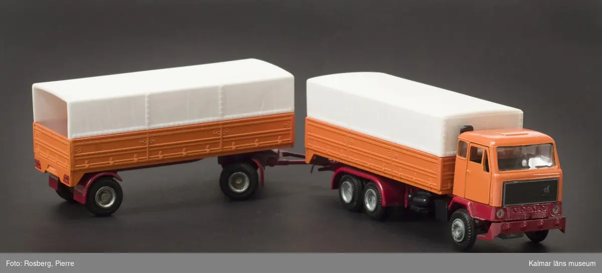 KLM 43929:4. Lastbil, av metall, vissa delar av plast, med släp. (Totalt 35 cm). Orange bil med vitt plastkapell, öppet bak, rött underrede.Text på motorhuv: Volvo. Text under: Nacoral, Made in Spain.