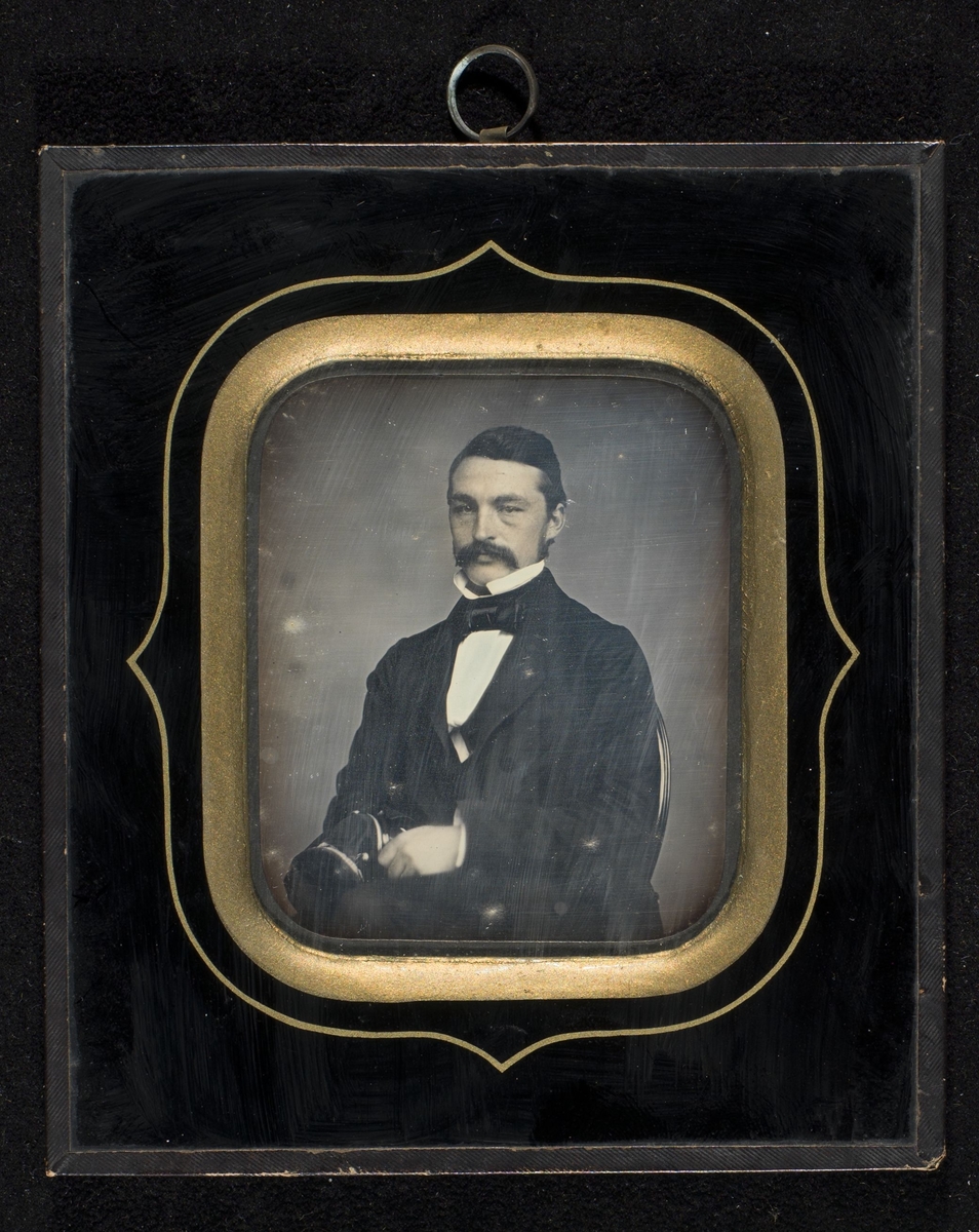 Portrett av mann innrammet bak glass og profilert passepartout. Opphengsring på baksiden.