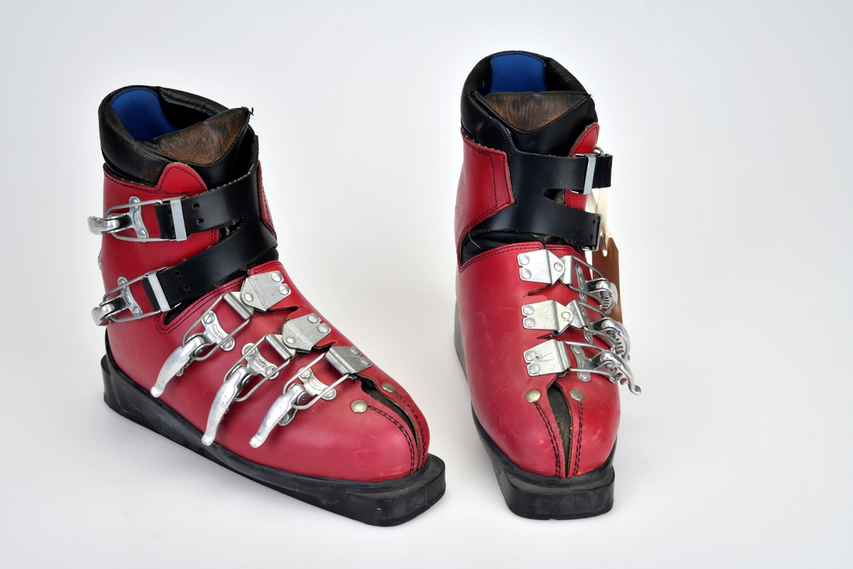 Et par slalomstøvler av merket "Humanic". De er røde med svarte detaljer. Materialet er lær og plast/gummi. Innvendig er de foret med blå ullfilt og blått syntetisk stoff. I skoene ligger det brune, tynne ullfiltsåler. Skoen er sydd av lær trukket med rød gummi. Kanten oppe på leggen er sydd av polstret svart lær. På tuppen av skoen er det laget en splitt i overtrekksmaterialet. På hver side av splitten er det sydd svarte sømmer og øverst er det "festet" med to nagler. Bak på skoen er det festet et sølvfarget metallskilt med blå tekst. Skoene har 5 spenner. De tre nederste er nede på skoen og begge deler av spennene er laget av metall. På leggen er det to spenner med reimer for stramming. Alle spennene har 5 hakk for ulik stramming. Sålen er av svart gummi. Den er avlang og er avrundet bak og noe mindre avrundet foran.