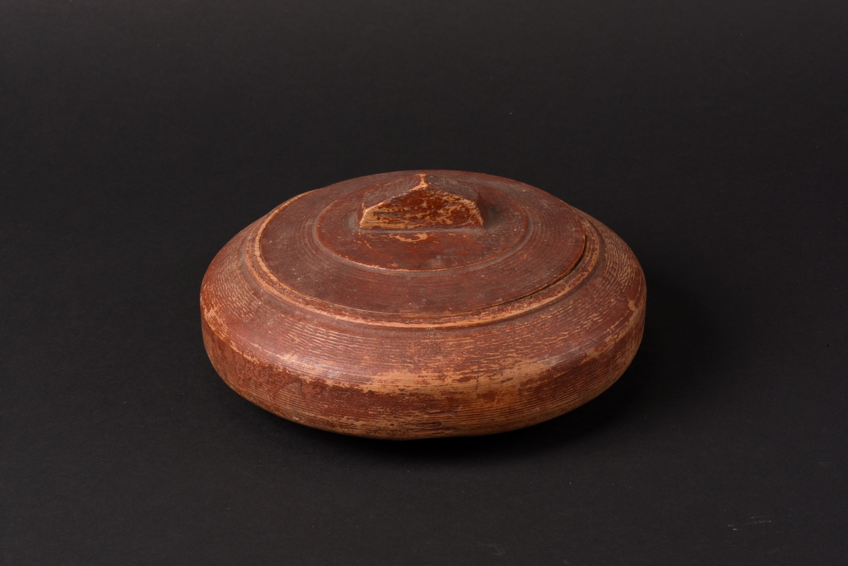 Rund svarvad smörask med lock, tillverkad av trä. Locket har en rektangulärt utskuren knopp som handtag.