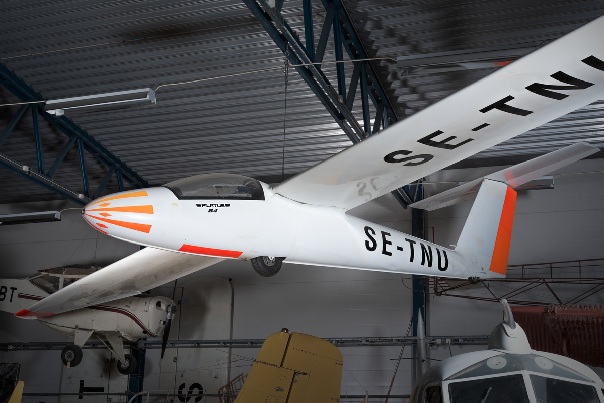 Segelflygplan av modell Pilatus B 4. Ensitsigt plan av plåt med vit flygkropp och vingar samt orange dekor.