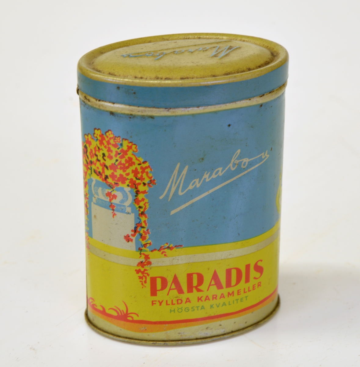 Marabou "Paradis fyllda karameller".
Flerfärgad. Påfågelmotiv.
Oval form.
