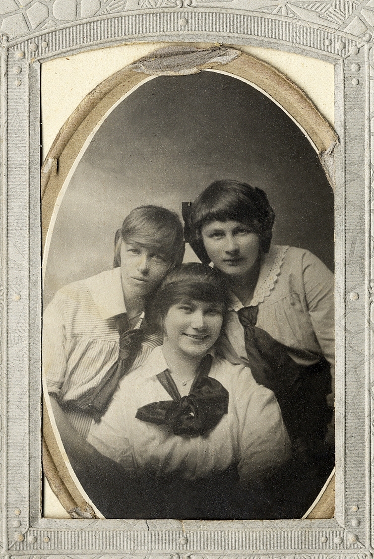 Tre tonårsflickor i blus och kjol. 
Knäbild. Ateljéfoto.

Fotografens äldsta dotter med väninnor.