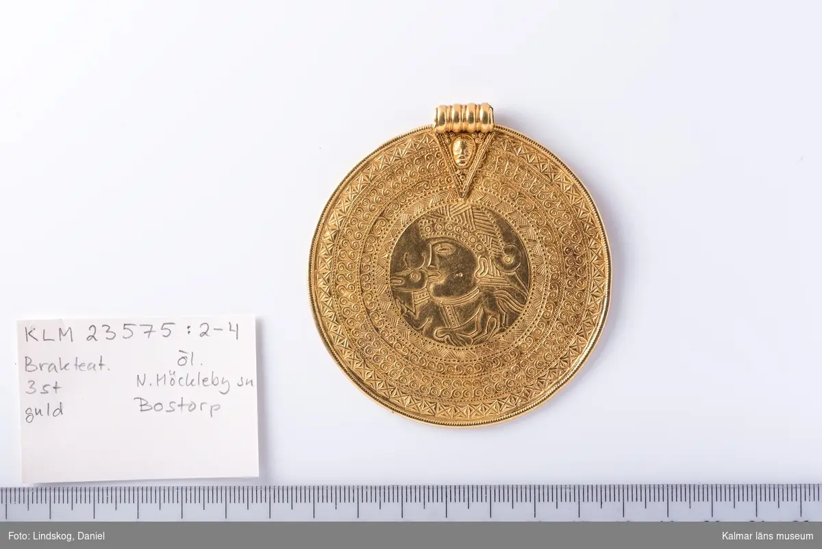 KLM 23575:2 Brakteat, av guld. Skatten ursprungligen nedlagd i en lerkruka av vilken fragment återfanns.