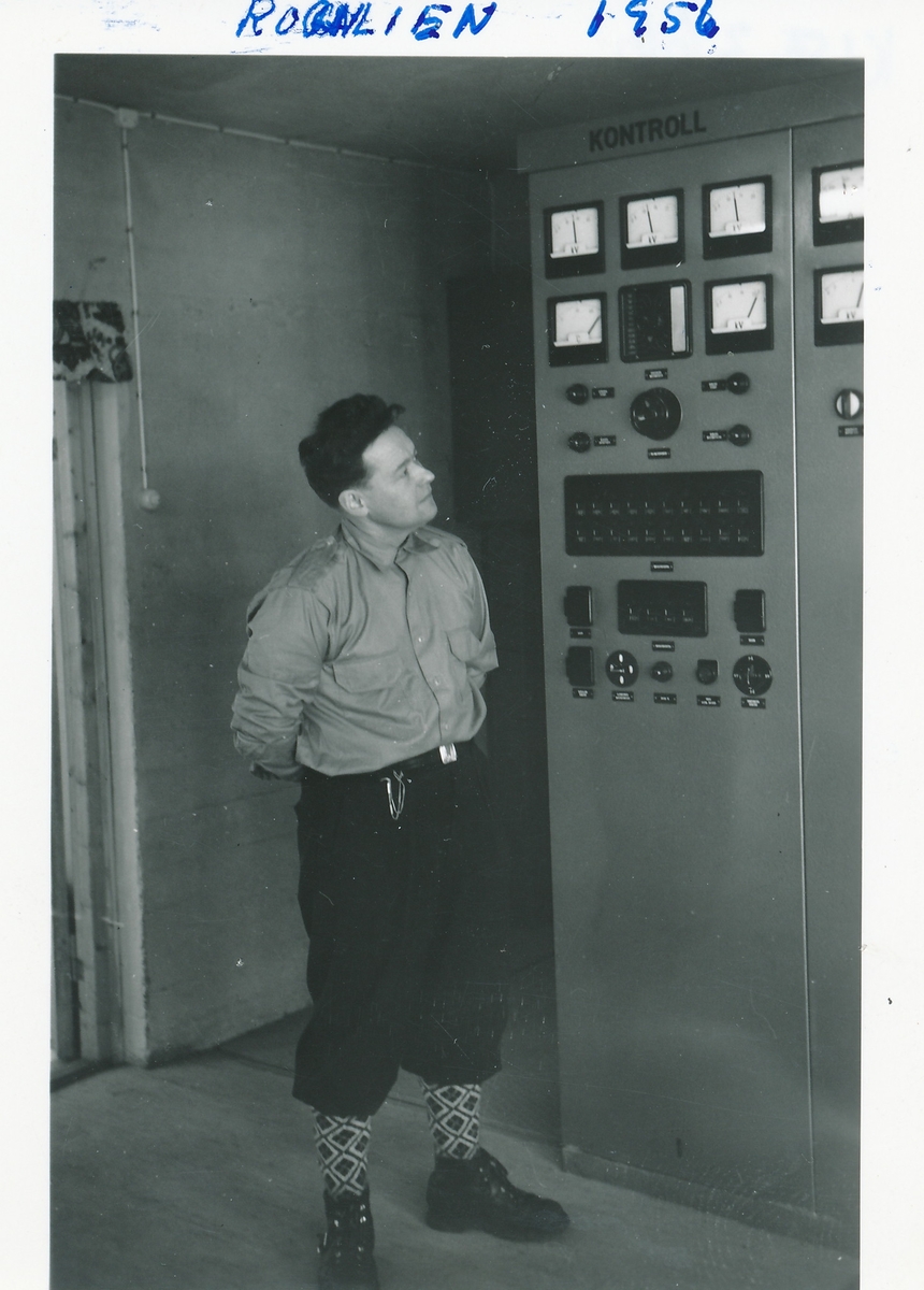 Mann iført skjorte, knickers og sportsstrømper ser på kontrollpanel i en av kraftstasjonene på Kistefoss.