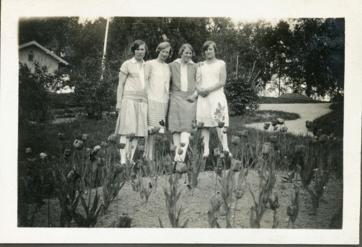 Elever fra husmorskolen på Skansgården, Kongsvinger, 1928. Fire unge kvinner i hagen bak et tulipanbed.