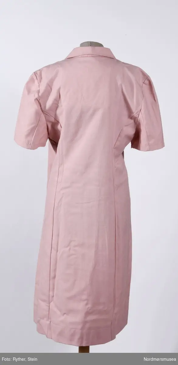 Rosa kjoleforkle med to dobbeltrader med knapper. Medfølger en liten plastpose på 19x22cm med ekstra stoff.