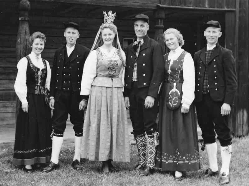 Seks unge kvinner og menn kledd i folkedrakter. Kvinnen i midten er kledd som brud med brudekrone.