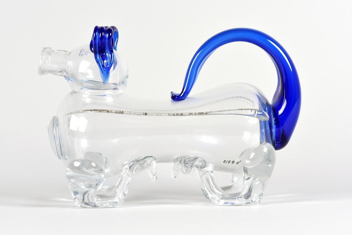 Brännvinsflaska i form av en hund, så kallad fyllehund. Tillverkad i klart och blått glas, svans och öron är blåa. Svansen fungerar som handtag.