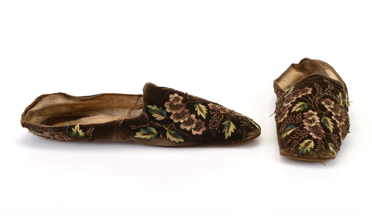 Et par damesko/tøfler sydd av brunsvart fløyel. På fløyelen er det brodert blomster og blader i ulike nyanser av lilla og grønt samt gråhvitt. Det er brodert med plattsøm og attersting. Det er også brodert på rikelig med metallperler som en gang har vært sølvfarget, men som nå er brun. Broderiene er både foran og bak på skoene
Innvendig er skoene foret med ubleket linstoff i den fremre delen av skoen. Den bakre delen er foret med skinn som en gang har vært hvit. Innersålen er av hvitt skinn. Yttersålen er av brunt lær. Skoene er firkantet foran og er helt flat.