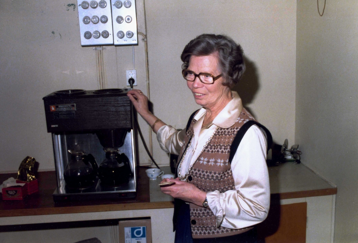 Alma Persson (1910 - 1987) står vid en kaffebryggare i Kommunalhusets kök, okänt årtal. Hon var socialdemokratisk politiker i Kållered samt arbetade i Lindgrens Lanthandel.