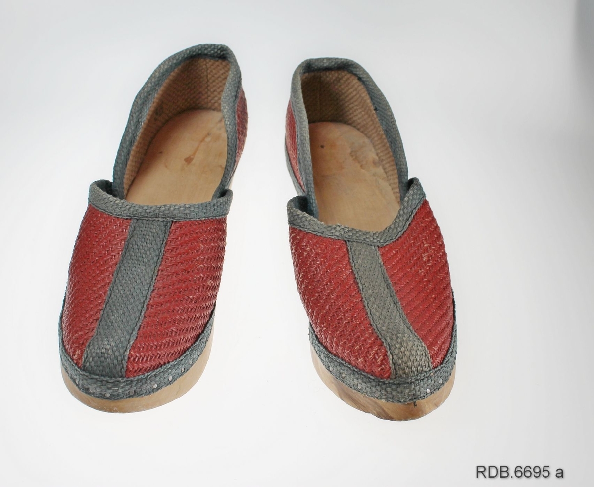 Et par damesko. Skoene er "krigsvare", fra 2. verdenskrig, med overlær av strie og tresåler (trebunner). Skoene er røde med grønne kantebånd. Foran på tåa, på hælen og rundt kanten på skoen er påsydd  forsterkninger av grønt striebånd. Rundt kanten er dette spikret fast til trebunnen. Skoene har kraftige trebunner med litt hæl og er ikke brukt. Venstre sko er str. 37, høgre sko str. 38.