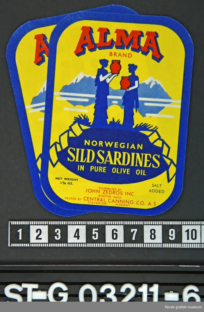Etikett i gul, rød og blå med siluetten av to kvinner med krukker i hendene foran et stilisert fjellandskap. 

"Norwegian sild sardines in pure olive oil"